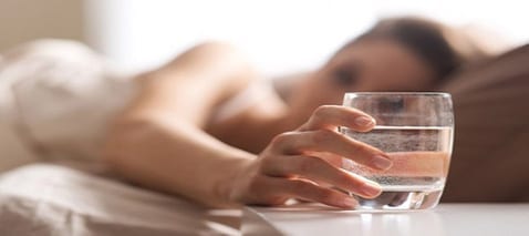 Jeune femme avec un verre d’eau sur sa table de nuit